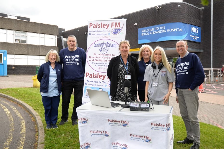 Members of Paisley FM, alongside NHS Greater Glasgow and Clyde’s Director for Clyde Melanie McColgan. They are standing behind a table, with an A-board behind them, in front of the Royal Alexandra Hospital.