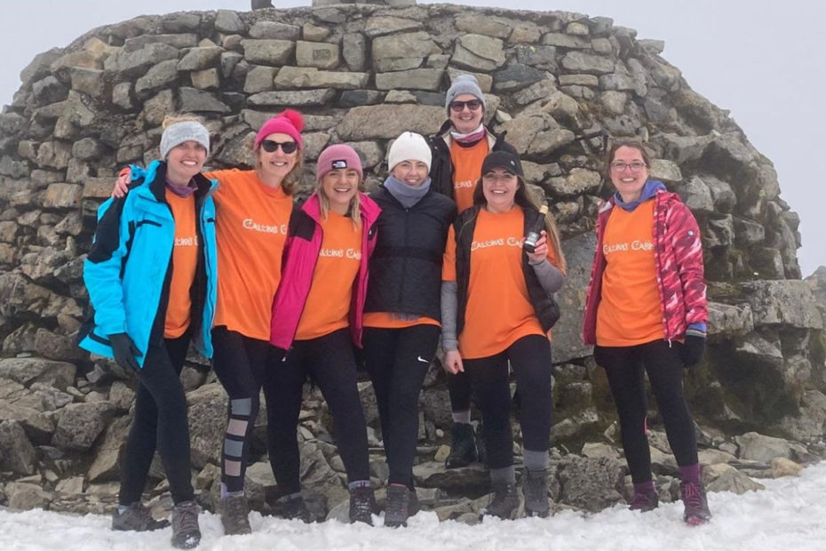 Seven members of the RHC team at the peak of a snow-covered Ben Nevis. They are smiling, wearing Calum's Cabin fundraising clothes.